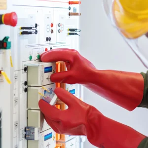 Elektriker mit Schutzhandschuhen und Helm führt Wartungsarbeiten an einer Schalttafel durch.