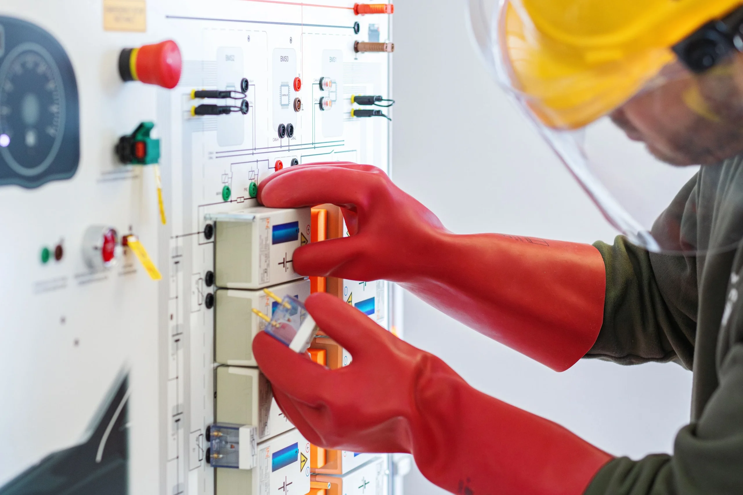 Elektriker mit Schutzhandschuhen und Helm führt Wartungsarbeiten an einer Schalttafel durch.